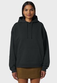 Čierna oversize mikina vyrobená z mäkkého materiálu, so sťahovacou kapucňou, prednou kapsou a rebrovanými manžetami. V kombinácii s hnedou sukňou.