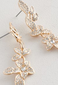 Ohrstecker in Goldoptik mit floralen Motiven und klaren Strasssteinen, mit Blatt- und Blumenmustern. Mit Stegen für sicheren Halt und strukturierten Details.