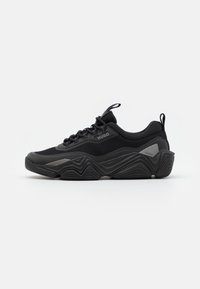 Scarpe da ginnastica nere con una parte superiore testurizzata, dotate di una suola spessa e ondulata e accenti tonali. I lacci e un pull tab completano il design.