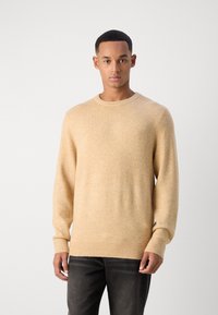Beige Wolle Pullover mit rundem Halsausschnitt, langen Ärmeln und gerippten Bündchen. Weiche Textur und lockere Passform, kombiniert mit dunkelgrauen Jeans.