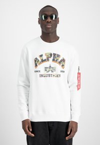 Felpa bianca con grafica "ALPHA INDUSTRIES" in multicolor, con colletto tondo e un'etichetta rossa con cerniera sulla manica.