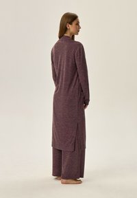 Długi fioletowy kardigan dziany w połączeniu z szerokimi fioletowymi spodniami. Posiada boczne rozcięcia dla swobody ruchu. Miękka tekstura, casualowy design.