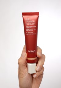 Tubo rojo de Kiko Milano Skin Trainer CC Blur con tapa blanca, etiquetado como "Medio". El texto en el tubo dice "Corrector Óptico de Piel Perfecta" en fuente blanca.
