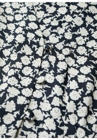 Tissu bleu marine avec imprimé floral blanc dense, comprenant des boutons recouverts de tissu le long d'une couture.