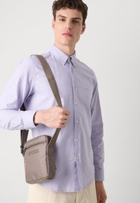 Lichtpaarse knopshirt met een kraag, gedragen met een lichtbruine schoudertas met ritssluiting en een ingebracht "BOSS" logo.