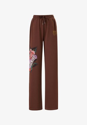 Hnědé tepláky vyrobené z měkké tkaniny, s velkým květinovým grafickým designem na jedné nohavici a elastickým pasem se šňůrkou.