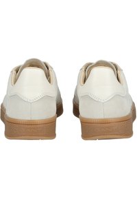 Zapatillas de ante blanco con suela de goma marrón, forma redondeada y talón de cuero liso en contraste. Presentan costuras mínimas y una marca discreta.