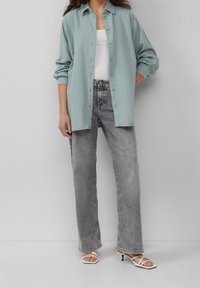 Lyseblå oversized skjorte i struktureret stof, båret over en hvid tanktop og kombineret med falmede grå jeans med lige ben og sandaler med stropper.