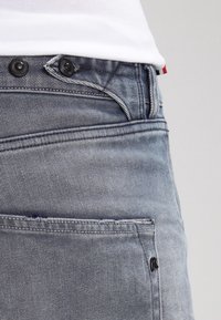 Harmaat denim-farkut, joissa on slim fit -malli, ja niissä on kaksi mustaa nappia sekä erottuva ommel. Mukana on takatasku, jossa on pieni logoyksityiskohta.
