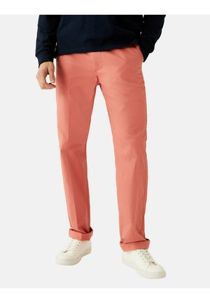 Pantalones de color coral hechos de tela ligera, con un diseño de pierna recta, puños enrollados y bolsillos delanteros, combinados con zapatillas blancas.