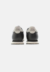 Scarpe da atletica nere con accenti bianchi, dotate di tomaia in pelle liscia, linguetta sul tallone a contrasto e testo stampato "DAL 1890" sul retro.