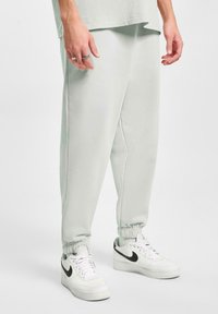 Pantalones deportivos gris claro con puños elásticos, que presentan un corte relajado y una textura suave, combinados con zapatillas Nike blancas.