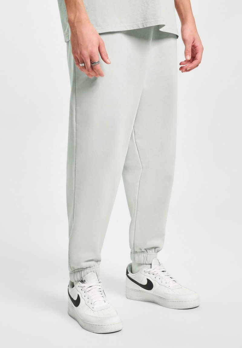 Pantalones deportivos gris claro con puños elásticos, que presentan un corte relajado y una textura suave, combinados con zapatillas Nike blancas.