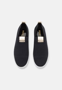 Ein Paar schwarze Strick-Slip-On-Sneaker mit weißen Sohlen und goldenen Michael Kors Logo-Tags auf der Vorderseite, von oben auf einem weißen Hintergrund betrachtet.