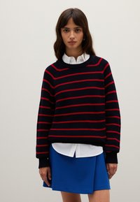 Maglione lavorato a maglia con righe orizzontali blu navy e rosse, scollatura tonda, polsini a costine, indossato sopra una camicia bianca con colletto e una gonna blu.