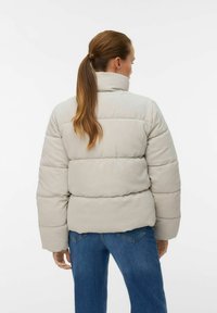 Doudoune en velours côtelé gris clair avec des côtes verticales, dotée d'un col montant et d'une silhouette oversize, associée à un jean en denim.