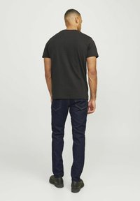 Schwarzes T-Shirt mit kurzen Ärmeln und rundem Halsausschnitt, kombiniert mit dunkelblauen Jeans. Der Stoff wirkt glatt, und die Passform ist lässig und entspannt.