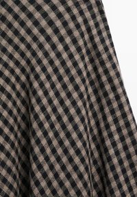 Schwarz-beige kariertes Gewebe mit strukturierter Oberfläche, das ein Gittermuster aus unterschiedlich großen Quadraten auf einem weichen Material zeigt.