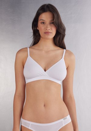 Witte bralette met een V-hals ontwerp, dunne bandjes en een naadloze afwerking. De stof lijkt zacht met een gladde textuur.