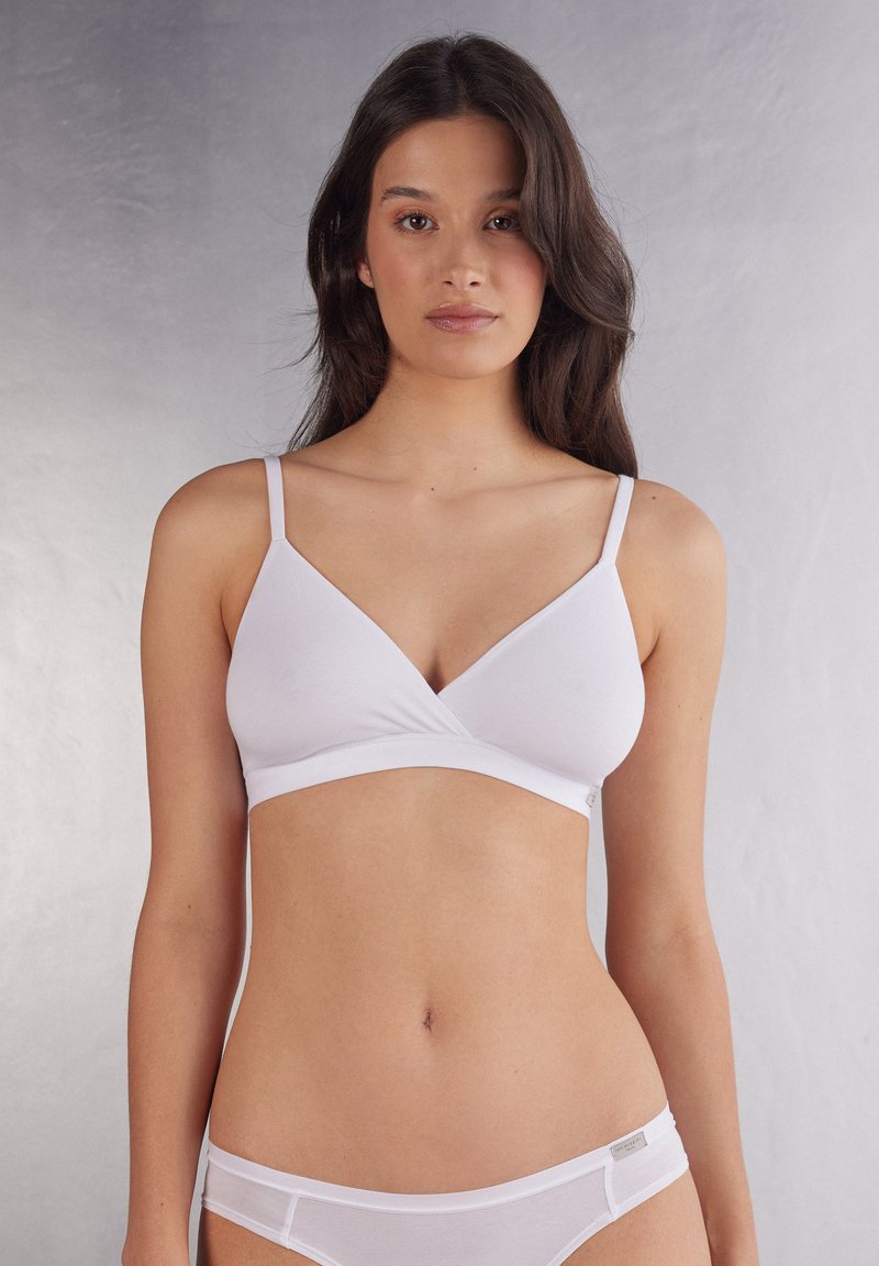 Vit bralette med V-ringning, tunna axelremmar och sömlös finish. Tyget verkar mjukt med en slät yta.