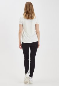 Camicia bianca a maniche corte abbinata a pantaloni neri aderenti e sneaker bianche, vista da dietro, che evidenzia il design semplice dell'abbigliamento.