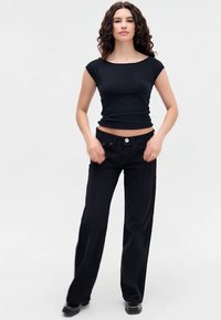 Zwarte aangesloten top met korte mouwen, gecombineerd met hoogafgezette zwarte wijde jeans, gepresenteerd op een model tegen een neutrale achtergrond.