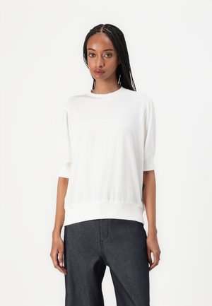 Hvit kortermet topp med rund hals og elastisk linning, laget av myk stoff; paret med mørk denim bukser.