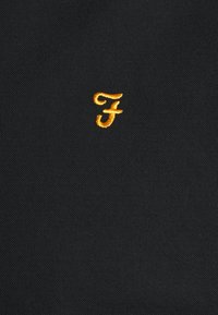 Black fabric with a textured weave features an embroidered yellow "F" logo positioned in the lower right corner.