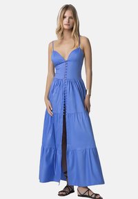 Lungo abito blu con bretelle sottili, corpino aderente e gonna a strati. Presenta una chiusura a bottoni sul davanti e uno spacco per facilitare i movimenti. Tessuto morbido.