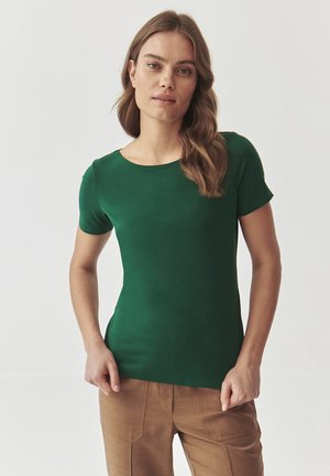 Kurzarm-T-Shirt in Grün aus glattem Stoff, mit Rundhalsausschnitt und tailliertem Schnitt, kombiniert mit beigen maßgeschneiderten Hosen.