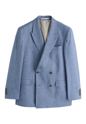 Mand iført lyseblå tekstureret blazer, hvid skjorte med tynde striber og olivengrøn slips med diskret mønster mod beige baggrund.