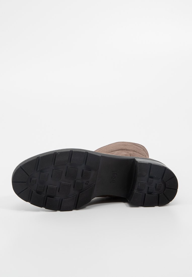 Braune Wildlederstiefel mit einer strukturierten schwarzen Gummisohle. Besitzt ein robustes Profilmuster für Grip und ein vereinfachtes, funktionales Design.