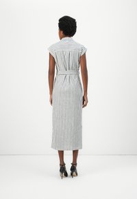 Rochie fără mâneci, cu dungi, având o talie marcată cu un cordon, cu dungi verticale alb-negru și o lungime până la jumătatea gambei, realizată dintr-un material ușor.