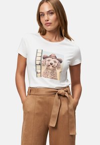 T-shirt blanc à manches courtes avec un graphique d'un chien portant un chapeau de cowboy marron, associé à un pantalon taille haute en beige avec une ceinture à nouer.