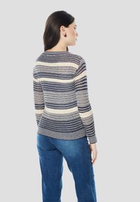 Oblečena pulover z mornarsko modrimi, kremnimi in bež vodoravnimi črtami. Ima dolge rokave, okrogel izrez in oprijet kroj.