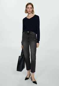 Črna dolga majica s V-izrezom, sivi hlače z visokim pasom, črna torbica in črne čevlje s koničastim prstom. Osredotočite se na uničen videz in prileganje denima.