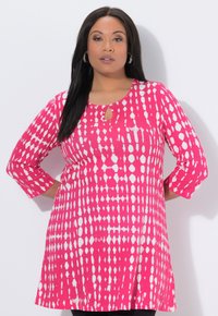 Jasnoróżowa tunika z białym wzorem, z dekoltem w kształcie łezki i rękawami długości do połowy przedramienia, wykonana z lekkiego materiału.