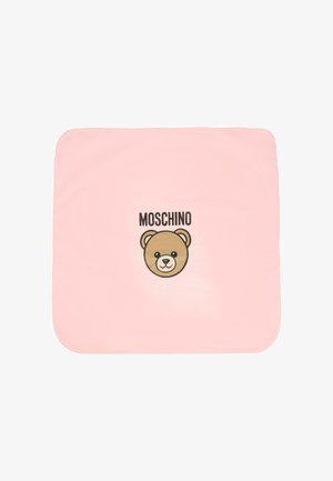 Różowy koc z rysunkiem twarzy misia i napisem "MOSCHINO" wydrukowanym powyżej w pogrubionym czarnym tekście. Gładki, miękki materiał. Kwadratowy kształt.