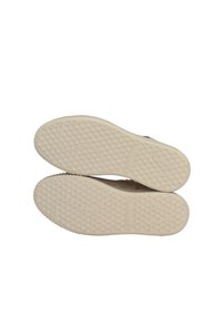 Beżowe gumowe podeszwy butów z wzorzystą teksturą i delikatnym bieżnikiem, z okrągłymi uchwytami i subtelnym oznaczeniem marki.