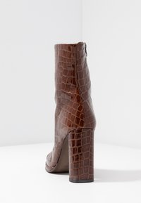 Bottine en cuir marron embossé crocodile avec un bout carré, un talon bloc haut et une fermeture éclair latérale. Texture lisse et brillante.
