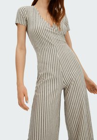 Combinaison rayée à manches courtes, décolleté en v et jambes larges. Présente des rayures noires sur un fond crème, en tissu texturé.