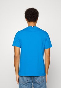 Blå T-shirt med korte ærmer og rund hals, med en lille stribet detalje ved halsen. Fremstillet af glat, let stof.