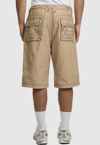 Beige Cargo-Shorts mit zwei Gesäßtaschen, kontrastierenden Nähten und einer lockeren Passform. Umgeschlagene Säume und strapazierfähiger Baumwollstoff.