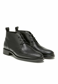Bottines en cuir noir avec une finition lisse, bout arrondi, empeigne à lacets, et accents de couture contrastés. Talon bas empilé.