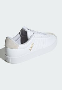 White leather sneakers with a textured finish, grey suede accents at the heel, and white rubber sole. Features subtle gold branding.