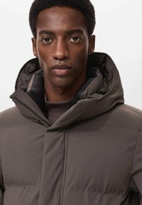 Giubbotto imbottito di colore grigio scuro, con colletto alto e cappuccio, leggero, con texture trapuntata, chiusura con zip e dettagli di design minimalisti.