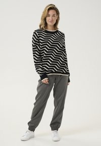 Black and white zigzag patterned knit sweater with long sleeves, paired with gray jogger pants and white sneakers on a plain background.