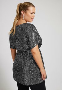 Top nero con paillettes, dalla vestibilità morbida, maniche corte e vita arricciata, con una texture liscia e dettagli scintillanti.