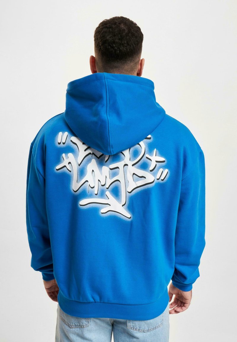 Hoodie en coton bleu avec un grand design de graffiti blanc au dos, doté d'une poche kangourou et de poignets et d'un ourlet côtelés.
