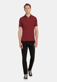 Bordowa koszulka polo w wąskim kroju, z krótkimi rękawami i dwoma guzikami przy kołnierzyku, zestawiona z czarnymi spodniami w wąskim kroju i czarnymi sneakersami.